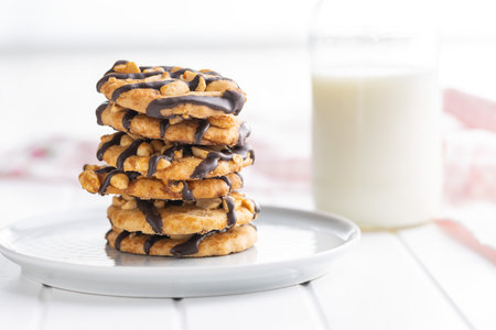 Chip cookies with peanuts and chocolate strips on a white table.