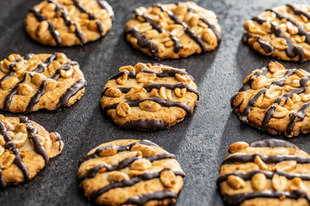 Chip cookies with peanuts and chocolate strips on a black table.