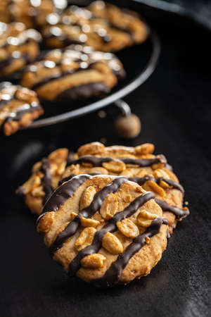 Chip cookies with peanuts and chocolate strips on a black table.