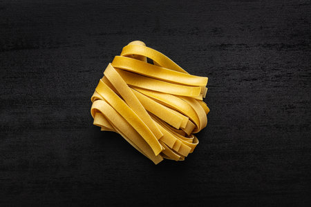 Uncooked pappardelle pasta on a black table. Top view.の写真素材