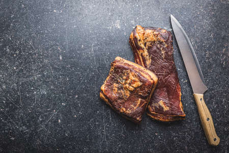 Whole smoked bacon on a black table. Top view.
