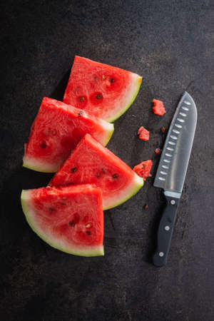 Slices of red watermelon with knife on a black table. Top view.の写真素材