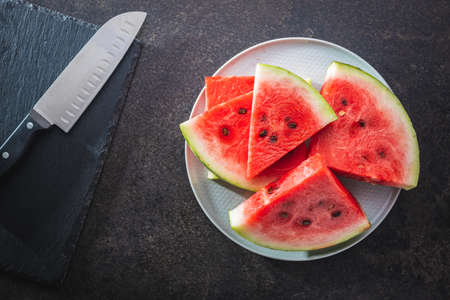 Slices of red watermelon with knife on a black table. Top view.