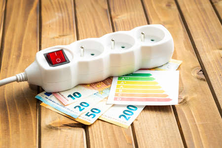 Electric socket, energy label and euro money on the wooden table. Concept of increasing electric...