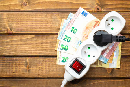 Electric socket and euro money on the wooden table. Concept of increasing electric prices. Top view.の写真素材