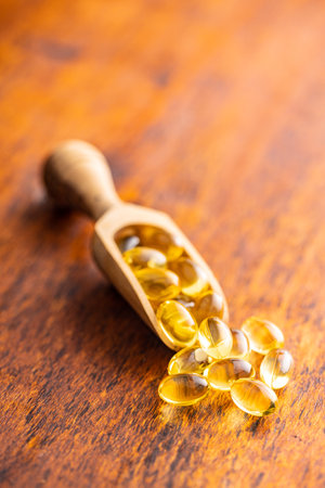 Fish oil capsules. Yellow omega 3 pills in wooden scoop on the wooden table.の写真素材