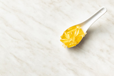 Fish oil capsules. Yellow omega 3 pills in spoon on the white table. Top view.の写真素材