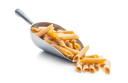 Uncooked whole grain pasta isolated on the white background. Raw penne pasta in scoop.の写真素材