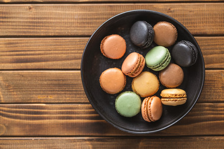 Sweet macaron dessert. Colorful macarons on a plate on the wooden table. Top view.の写真素材