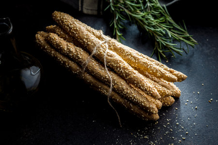 Italian grissini bread sticks with sesame seeds on the black table.