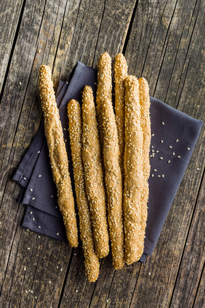 Italian grissini bread sticks with sesame seeds on the wooden kitchen table. Top view.
