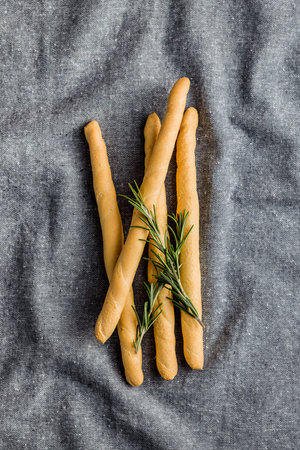 Italian grissini bread sticks and rosemary on the kitchen tablecloth. Top view.