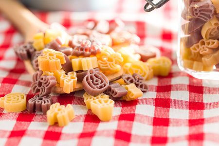 Pasta of various scary shapes. Uncooked halloween pasta in spoon on a checkered tablecloth.の写真素材