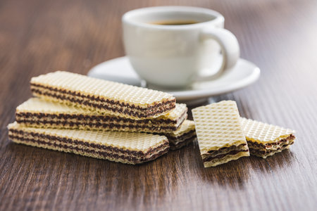 Sweet chocolate wafer and coffee cup on the wooden table.