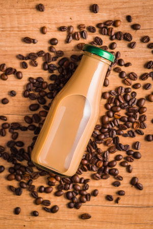 Coffee milk in glass bottle and coffee beans on the wooden table.の写真素材