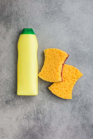 Sponge for washing dishes, plastic bottle and plates on the gray kitchen table. Top view.の写真素材