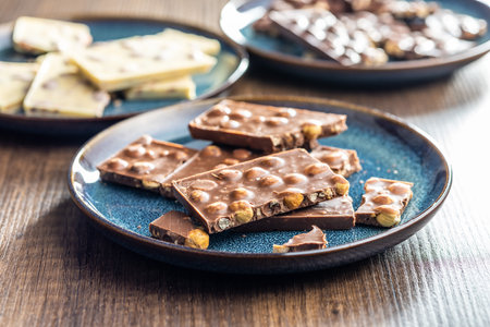 Broken chocolate bars with nuts on the wooden table.の写真素材