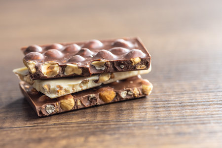 Broken chocolate bars with nuts on the wooden table.