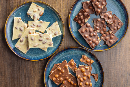 Broken chocolate bars with nuts on the wooden table. Top view.の写真素材