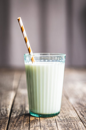Glass of milk with striped straw on the wooden table.の写真素材