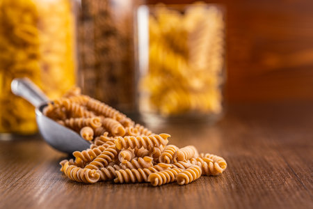 Raw whole grain fusilli pasta. Uncooked pasta in scoop on the wooden table.の写真素材