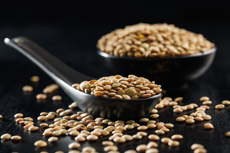 Uncooked lentil legumes in ceramic spoon on the black table.の写真素材