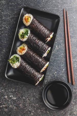 A black plate with sushi pieces with accompanying chopsticks and a bowl of soy sauce. The sushi shows a variety of colors, textures, and fillings, showcasing the artistry of Japanese cuisine.の写真素材