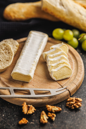 Brie cheese wedge styled on a wooden cheese board accompanied by fresh French bread and grapes for a...