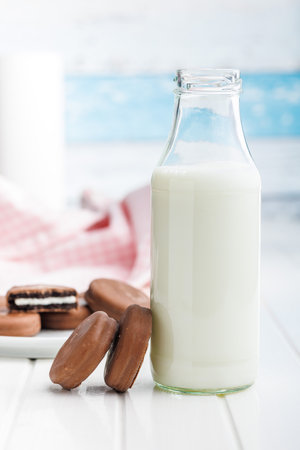 Chocolate Covered Cookies and Glass of Milk on a white table.の写真素材
