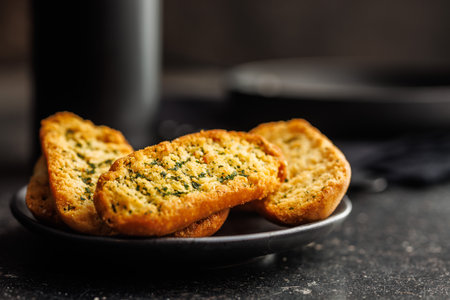 Garlic crisp bread Slices Topped With Herbs on plate on a black table.の写真素材