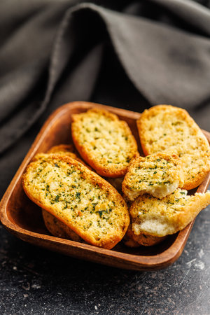 Garlic crisp bread Slices Topped With Herbs in a bowl on a black table.の写真素材