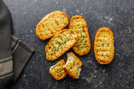 Garlic crisp bread Slices Topped With Herbs on a black table. Top view.の写真素材