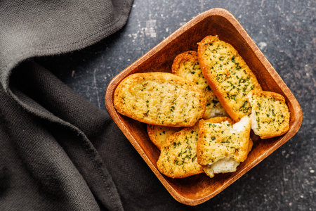 Garlic crisp bread Slices Topped With Herbs in a bowl on a black table. Top view.の写真素材