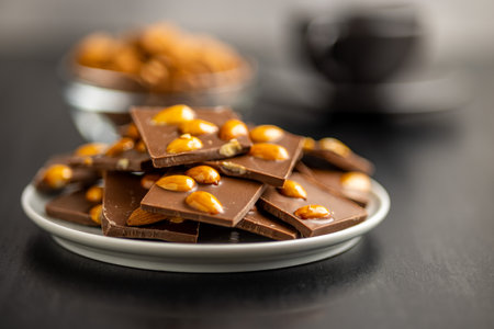 Broken chocolate bar with almonds on a plate on a black table.