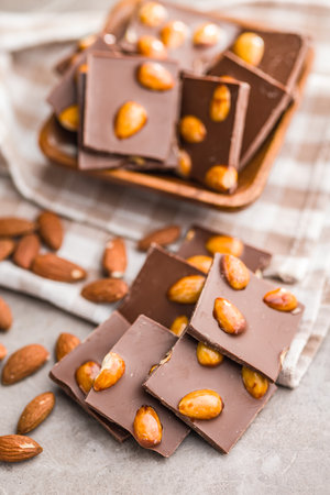 Broken chocolate bar with almonds on a kitchen table.の写真素材