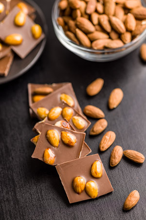 Broken chocolate bar with almonds on a black table.の写真素材