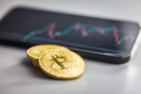 Bitcoin gold coin on a gray background. Cryptocurrency and business chart in cellphone.の写真素材