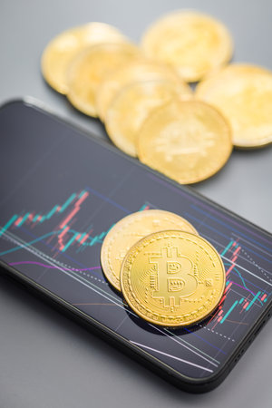 Bitcoin gold coin on a gray background. Cryptocurrency and business chart in cellphone.の写真素材