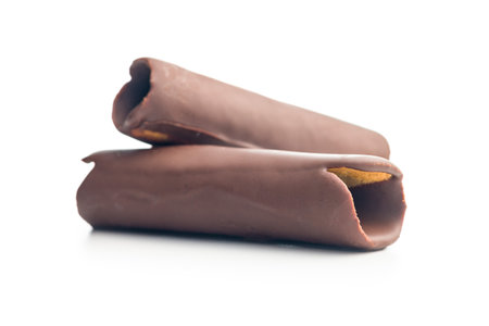 Chocolate covered wafer rolls stacked on top of each other on a white background. The rolls are a...