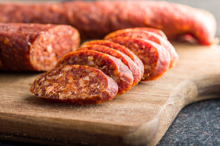 Sliced smoked salami sausage on a wooden cutting board.の写真素材
