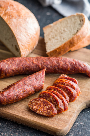 Sliced smoked salami sausage on wooden cutting board on a black table.の写真素材