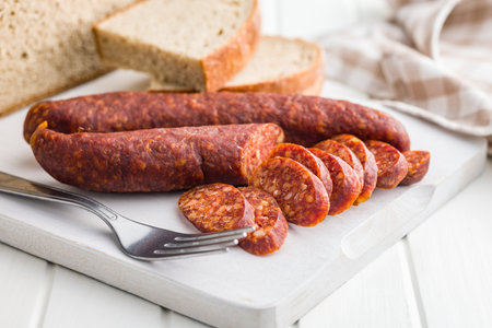 Sliced smoked salami sausage on wooden cutting board on a white table.の写真素材