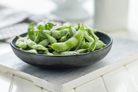 Green edamame pods. Fresh soybeans in a plate on a white cutting board.