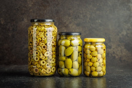 Pickled green olives in brine in a jar on a black table.の写真素材