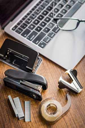 Office equipment. Stapler, staple remover, tape dispenser and hole puncher on a wooden table.の写真素材