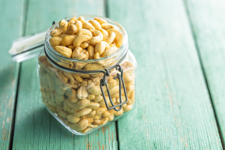 Roasted cashew nuts in a jar on a green wooden table.の写真素材