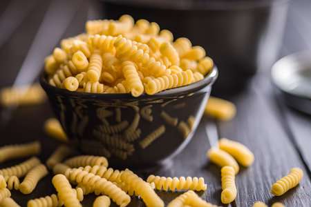 Uncooked italian pasta. Fusilli pasta in bowl on a black table.の写真素材