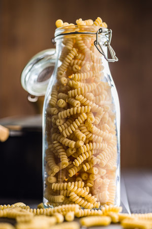 Uncooked italian pasta. Fusilli pasta in glass bottle on a black table.の写真素材