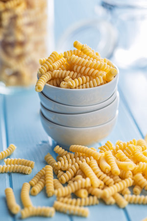 Uncooked italian pasta. Fusilli pasta in bowl on a blue table.の写真素材
