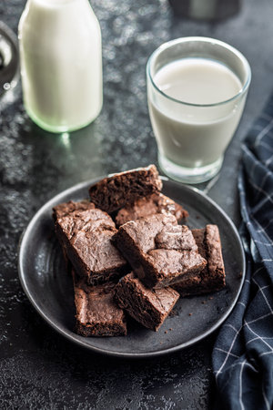 Homemade chocolate brownies on a plate and glass of milk on a black table.の写真素材